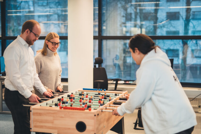 Kolme Teamitin työntekijää pelaamassa pöytäjalkapalloa.