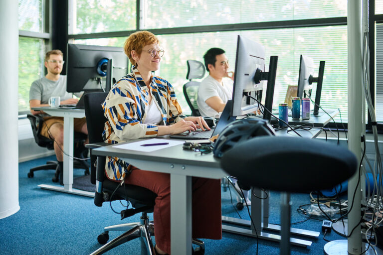 Three people sitting at Teamit office at their computers, smiling and working